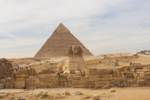 Rappresentazione iconica della Sfinge di Giza, con la maestosa Piramide di Giza sullo sfondo. La Sfinge, con il suo volto enigmatico e il corpo di leone, guarda silenziosa verso l'orizzonte, testimone della grandezza dell'antico Egitto.